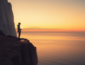 Person standing on a cliff at sunrise, holding a glowing light, symbolizing hope and renewal.